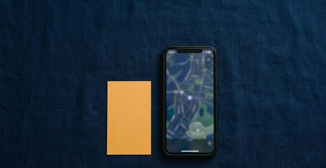A smartphone showing a blurred map interface on a dark surface beside a blank amber business card.