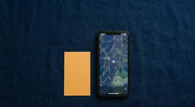 A smartphone showing a blurred map interface on a dark surface beside a blank amber business card.