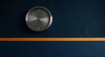 A softly blurred analog clock face behind a sharp horizontal amber line bisecting the frame.
